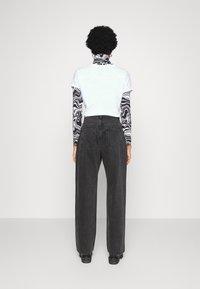 Vaqueros anchos negros de cintura alta, combinados con una camiseta blanca de manga corta sobre una blusa de manga larga con un estampado en blanco y negro.