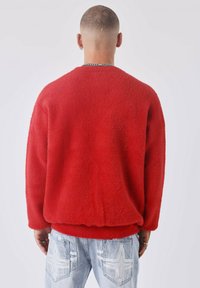 Rode, oversized fleece trui met een ronde halslijn, geribbelde manchetten en zoom. Gepaard met lichtblauwe jeans met stervormige accenten.