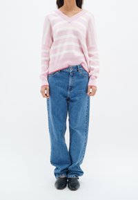 Pull-over V à rayures rose clair et blanches associé à un jean bleu taille haute et des chaussures noires, avec une coupe décontractée et une jambe droite.