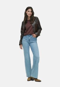 Brun læder cropped jakke over en bordeaux skjorte, parret med lyseblå flagrende jeans og brune ankelstøvler. Enkel, klassisk design.