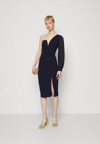 Robe bleu marine avec un design à une épaule, dotée d'un décolleté en V profond et d'une longue manche translucide, avec une fente haute sur la cuisse et une coupe ajustée.