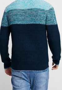 Stickad tröja med en gradient av turkos och mörkblå nyanser. Strukturerad tyg med ribbade muddar och fåll. Avslappnad passform.