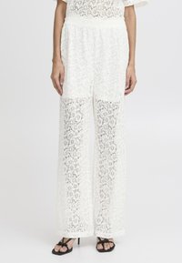 Vita spets palazzo-byxor med en vid bendesign, blommönster och elastisk midja. Genomskinlig textur, kombinerat med svarta sandaler.