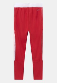 Czerwone sportowe legginsy z białym elastycznym pasem, ozdobione białymi bocznymi paskami i wykonane z gładkiego, elastycznego materiału zapewniającego komfort.