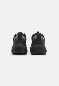 Black athletic shoes with a textured fabric upper, padded collar, elastic laces, and a chunky rubber sole. Logo embossed on heel.