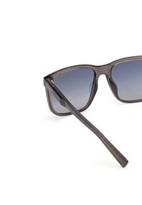 Gafas de sol de color gris oscuro con un marco triangular, lentes grises degradados y brazos de plástico elegantes con una sección de agarre texturizada.