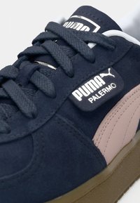 Navy suede sneaker with a pink leather stripe, rubber sole, and black laces. Features a branded tongue and a textured outsole for grip.