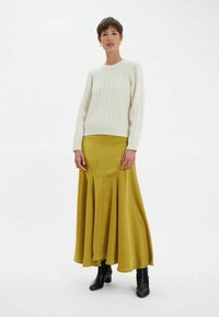 Pull en maille blanche associé à une longue jupe fluide en satin jaune moutarde et des bottines noires. Texture lisse, haut ajusté, bas évasé.