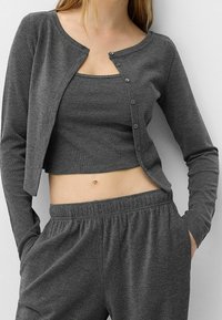 Grå långärmad cardigan med rundad halsringning och fem knapplistningar, bärs över en matchande ribbad linne och byxor med elastisk midja.