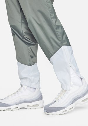 Lettræ kundefrugtfuld, tofarvet nylon træningsbukser i grå og hvid med lynlåschaneller ved anklerne, parret med lagdelte sneakers i hvid og grå.