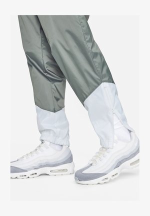 Lekkie, dwukolorowe spodnie dresowe z nylonu w odcieniach szaro-białych z zamkami błyskawicznymi przy kostkach, w połączeniu z białymi i szarymi sneakersami warstwowymi.