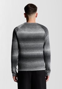 Grau geripptes Sweatshirt mit einem Farbverlauf-Design in dunkleren und helleren Tönen. Lange Ärmel und ein runder Halsausschnitt sind sichtbar.