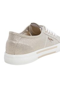 Baskets en toile beige avec un motif rayé texturé, semelle en caoutchouc blanc et lacets ronds. Présente des accents cousus le long du talon.