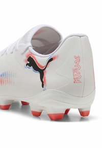 Clé haute de football Puma en blanc avec des accents rouges et bleus, présentant une tige texturée, un logo noir et des crampons à bouts roses.