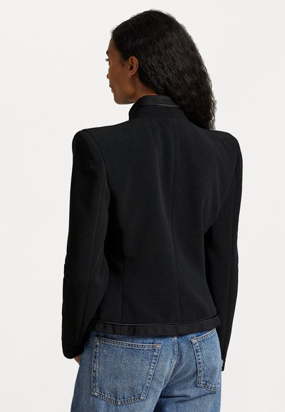 Μαύρο σακάκι με δομημένο σχέδιο, που διαθέτει ψηλό γιακά και υφασμάτινη υφή. Συνδυασμένο με ψηλοκάβαλες μπλε τζιν.