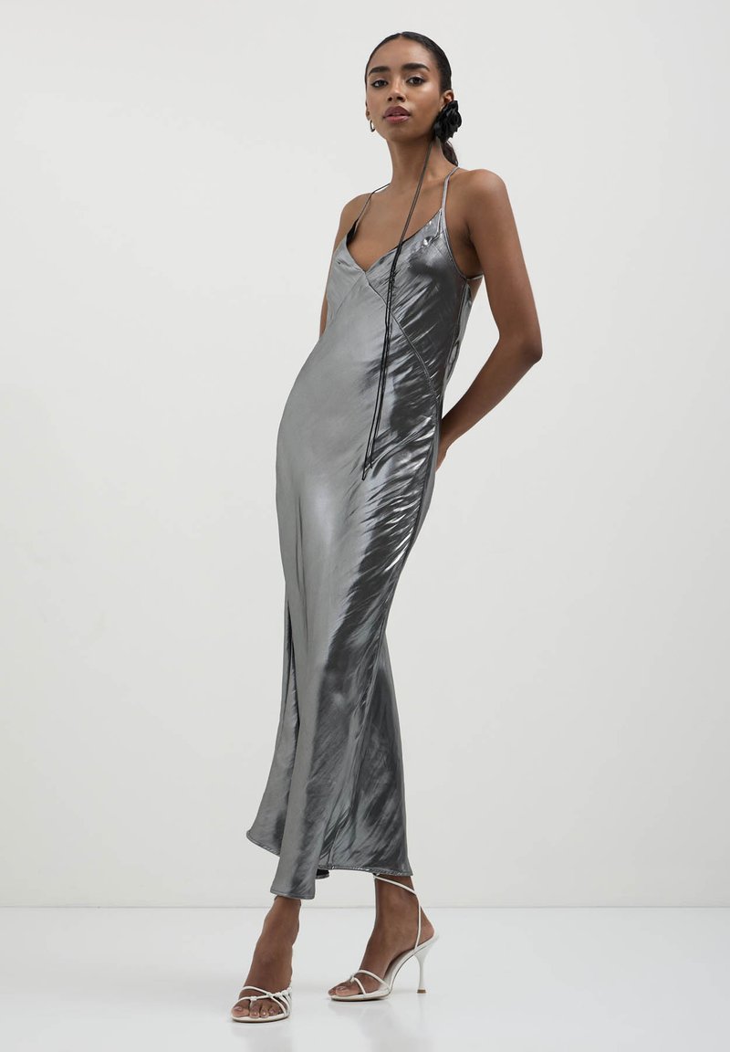 Silbernes Satin-Slip-Kleid mit dünnen Trägern, einer taillierten Silhouette und einem seitlichen Schlitz, das eine glatte, reflektierende Textur präsentiert.