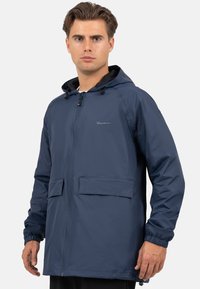 Marineblauwe waterdichte jas van lichtgewicht materiaal, met een capuchon, elastische manchetten, twee voorzakken en een volledige ritsluiting.