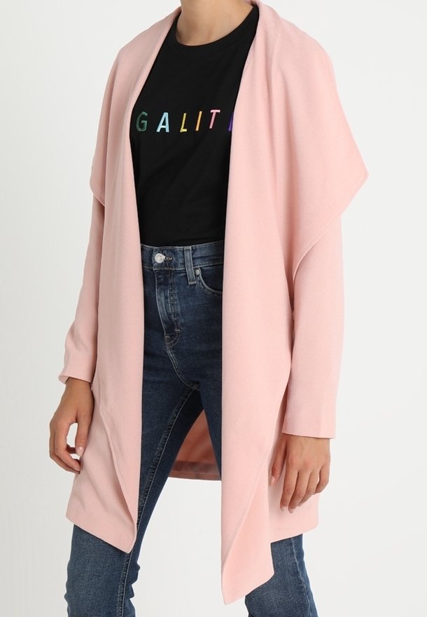 Cardigan rosa chiaro aperto sul davanti in un tessuto morbido, con maniche lunghe e una vestibilità rilassata, indossato sopra una maglietta nera con scritte colorate.