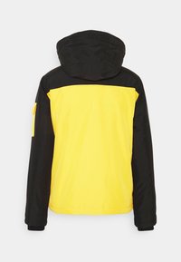 Czarna i żółta kurtka z kapturem, z czarną górną częścią i żółtą dolną, z kieszenią na lewym rękawie. Gładka tekstura.