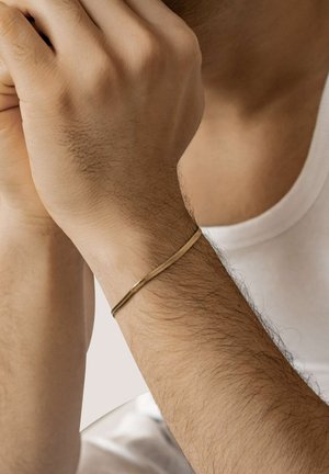 Gold-toned metal bracelet worn on a wrist, featuring a smooth, cylindrical design. The skin is visible with natural hair texture.