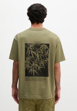 Man wearing olive green T-shirt with black bamboo leaf print and text on the back, paired with matching patterned shorts, facing away.