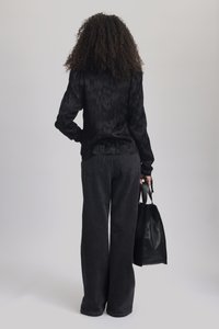 Blusa nera a maniche lunghe con un motivo testurizzato, abbinata a pantaloni larghi in denim nero a vita alta. Borsa tote in pelle nera tenuta in mano.