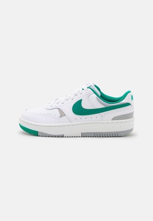 Bílé nízké tenisky s zeleným swooshem Nike, akcenty a vnitřním podšívkou, s šedými detaily a bílými šňůrkami na ploché podrážce.