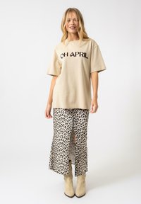 Camiseta de algodón beige con el texto negro "OH APRIL", combinada con una falda de estampado de leopardo con una abertura frontal, complementada con botines de tobillo beige claros.