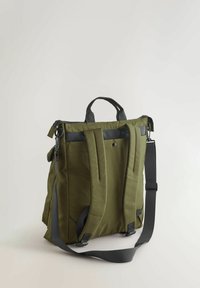 Zelen nahrbtnik iz tkanine z dvojno ročico za nošenje, nastavljivimi naramnicami in zgornjim zapiranjem z zadrgo. Ima trdne šive in minimalno kovinsko opremo.