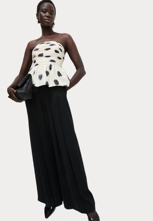 Strapless peplum top in cream with black splashes, paired with black wide-leg trousers. Model holds a black textured clutch.