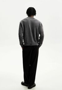 Szary sweter dziany z widocznym przetarciem, ściągaczami na mankietach i dolnym brzegu. W połączeniu z czarnymi spodniami i gładkimi czarnymi butami, widziany od tyłu.