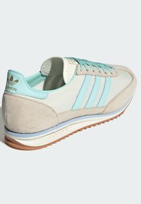 Baskets Adidas avec un dessus bleu clair et crème, des détails en daim, un design à trois bandes et une semelle en gomme texturée.