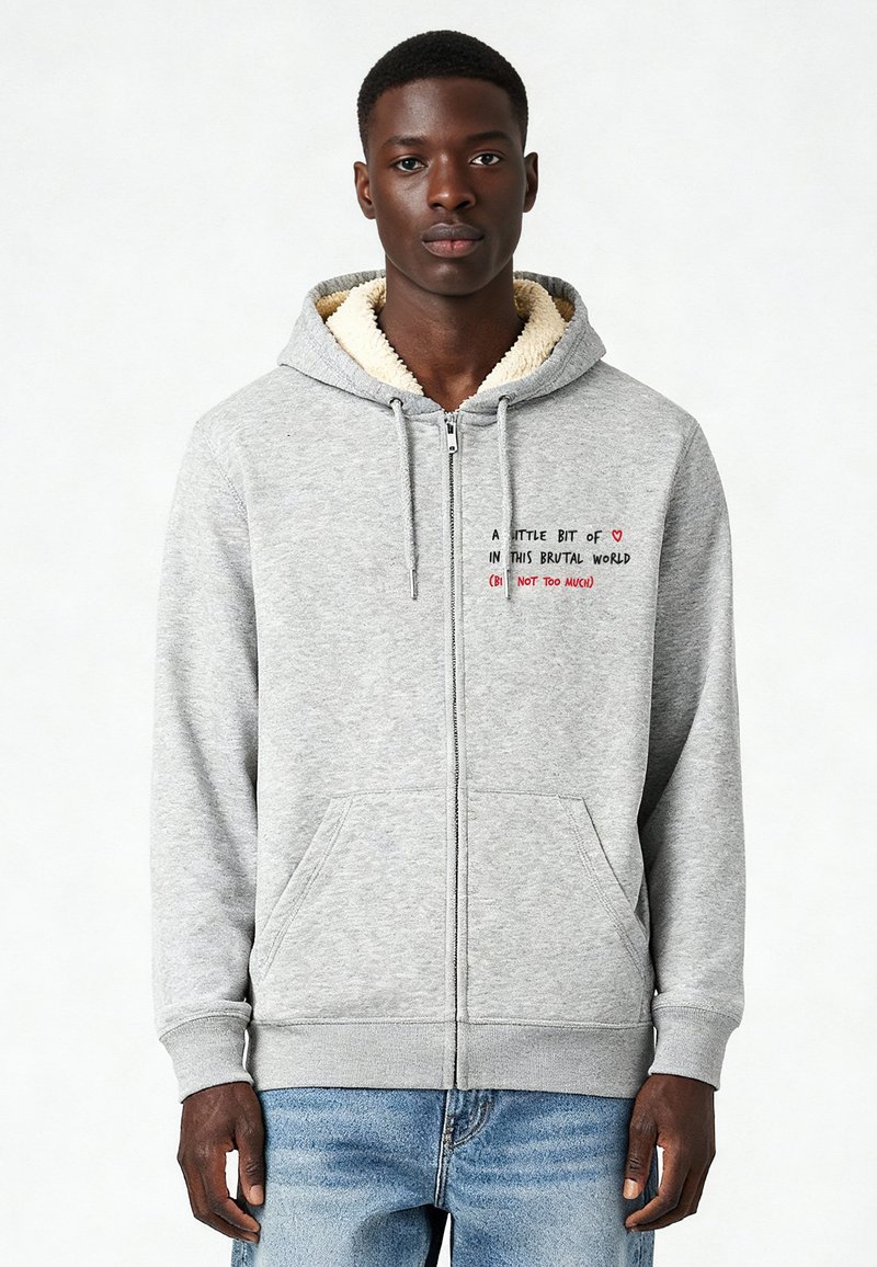 Grijze ritssluiting hoodie met een zachte, crème-kleurige fleece voering. Voorzien van voorzakken en geborduurde tekst in het rood en zwart op de borst.
