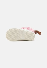 Botte en caoutchouc rose avec des motifs de cœur, semelle texturée blanche et accent en cuir brun. Dispose d'un bout arrondi et d'une finition lisse.