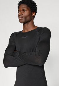 Czarna bluzka z długim rękawem i okrągłym dekoltem, wykonana z lekkiego, gładkiego materiału. Posiada subtelne logo oraz dopasowany krój podkreślający rękawy.