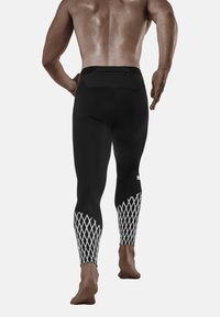 Zwarte sportleggings met een gestructureerd wit diamantpatroon op de onderbenen, voorzien van een veilige achterzak in de tailleband.