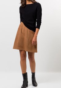 Zwarte gebreide trui met lange mouwen, gecombineerd met een bruine suède A-lijn rok, voorzien van een zijzak. Zwarte enkellaarsjes maken de outfit af.