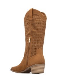 Bota alta hasta la rodilla de ante perforado en color camel, con un tacón ligero, cierre lateral con cremallera y un lazo en la parte superior para facilitar su colocación.