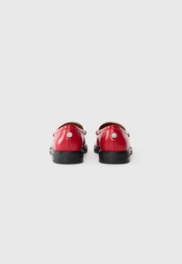 Red leather shoes with a smooth texture, rounded shape, and black rubber soles. Features silver accents on the back.
