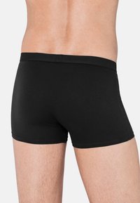 Boxers en coton noir avec une taille douce, un design ajusté et une texture lisse. Présente des coutures décoratives le long des bords.