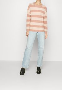 Pull en maille rayé rose et crème avec un col rond, associé à un jean droit bleu clair et des chaussures noires à enfiler.