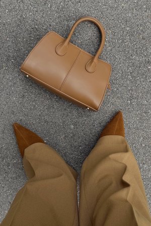 Sac à main en cuir marron avec un design structuré, deux poignées arrondies et des coutures contrastées, posé sur une surface grise texturée.