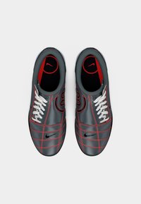 Ζευγάρι γκρι και κόκκινων ποδοσφαιρικών παπουτσιών Nike με λευκά κορδόνια, μαύρα λογότυπα Nike και κόκκινες ραφές, σε θέαση από πάνω σε λευκό φόντο.