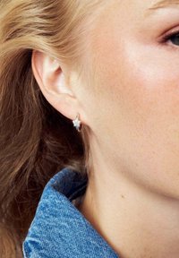 Silverring med stjärndesign, utsmyckad med små klara stenar. Bakgrunden inkluderar en denimkrage och vågigt hår.