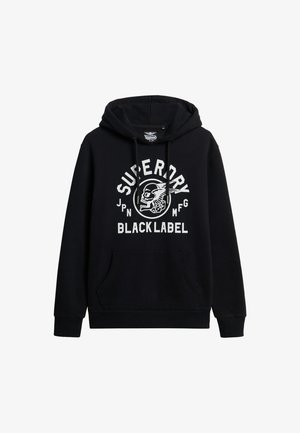 Felpa nera con cappuccio, tasca frontale e cappuccio regolabile tramite cordino. La scritta bianca presenta "Superdry" e una grafica di teschio. Tessuto misto cotone.