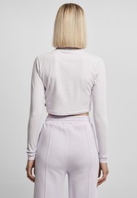 Langermet, kort topp i myk lavendelstoff, kombinert med matchende høyt midje lavendel joggebukser; glatt tekstur, elastisk midjebånd.