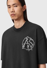 Zwarte oversized t-shirt gemaakt van katoen, met een witte grafiek van botten in een cirkelontwerp op de linkerborst.