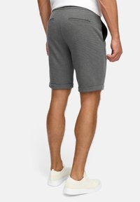 Shorts gris en tissu texturé, avec des revers roulés et deux poches arrière ; associés à des baskets blanches sur un fond uni.