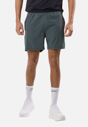 Man wearing dark gray athletic shorts, white crew socks with black text, and white sneakers standing against a plain background.