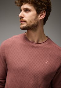 Sweatshirt aus Waffelstrick in staubigem Rosa, mit Rundhalsausschnitt und einem dezenten Logo-Patch auf der Brust, bietet ein strukturierteres Erscheinungsbild.